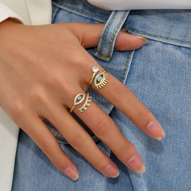 main posée sur un jeans portant bague dorée avec symbole du mauvais oeil et ornée de strass type diamant 